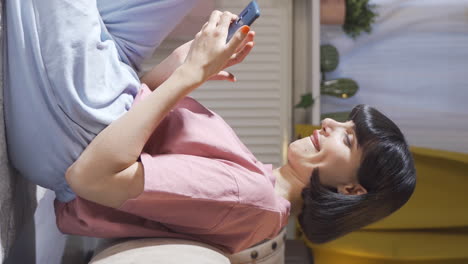 Vertical-video-of-Young-woman-using-phone-with-happy-expression.-The-young-woman-is-enjoying-it.
